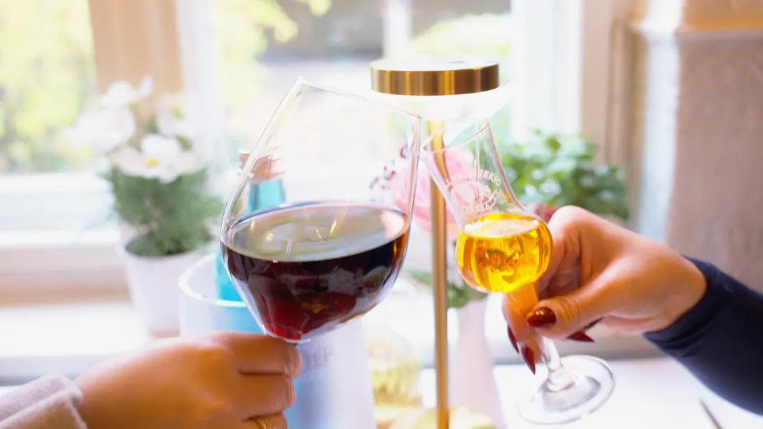 Zwei Gäste stoßen mit Rotwein und einem Schnaps an