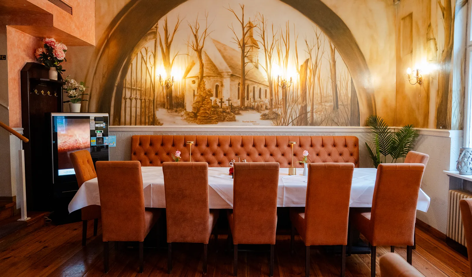 Lange Tafel mit Polsterbank vor einem Wandbild